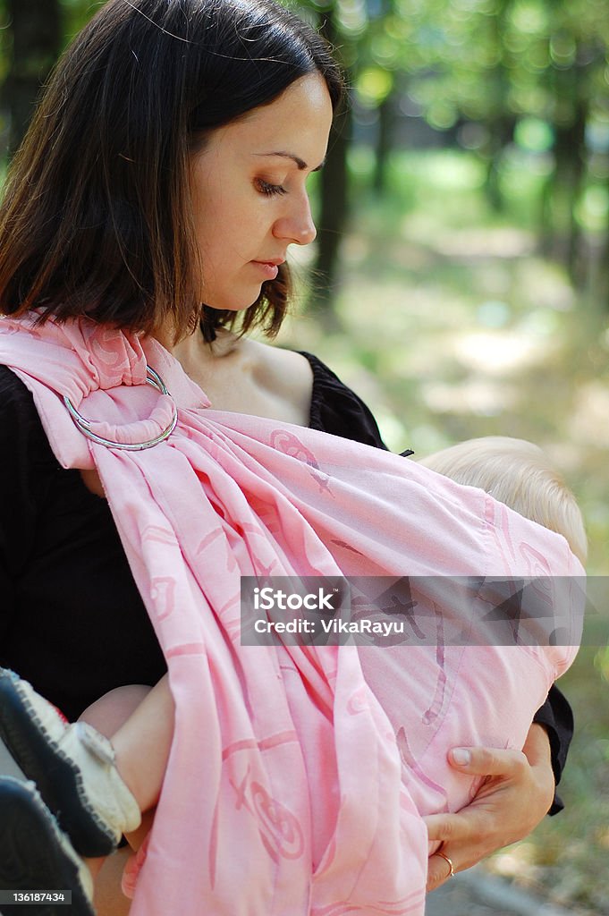 Breastfeeding baby in a sling Young mother breastfeeding her baby boy while holding him in a baby carrier Breastfeeding Stock Photo