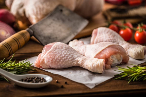 Group of raw chicken legs on a rustic wooden table Front view of three raw chicken legs disposed on a wax paper surrounded by some cherry tomatoes, rosemary, pepper and a meat cleaver. All the objects are on a rustic wooden table. chicken leg stock pictures, royalty-free photos & images