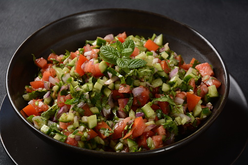 Shirazi Salad with tomatoes, cucumbers, red onions, parsley and mint with fresh lemon juice in a black bowl. Persian Shirazi vegetable salad closeup. Popular Israeli food