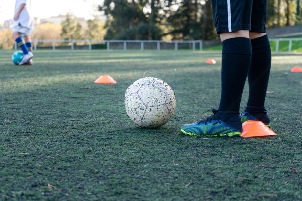 istock Unrecognizable children practicing soccer on an artificial turf field, both with a ball at their feet to start training using colored cones. 1361878626