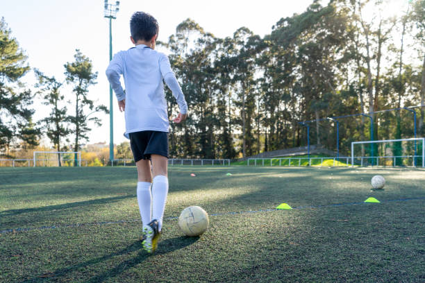 Child with his back to a soccer practice on a sunny day on an artificial turf field. Colored cones demarcating the practice to improve the use of the ball. Concept of sport for children. stock photo
