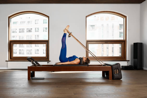 The instructor does exercises on the reformer, a beautiful girl trains on the modern reformer simulator to work out deep muscles, the modernized reformer equipment for Pilates and yoga stock photo