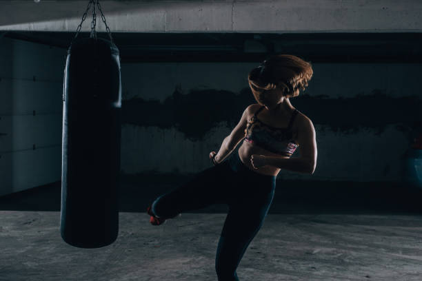 istock Young silhouette female practicing high kick with the boxing bag inside the garage. 1361893328
