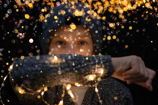 Boy with knitted sweater staying on the black background and looking at golden lights and bokeh