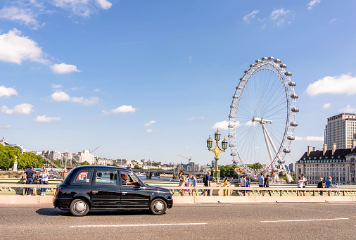 London, UK - A black cab crossing the Thames on Westminster Bridge in central London, with the London Eye on the horizon.