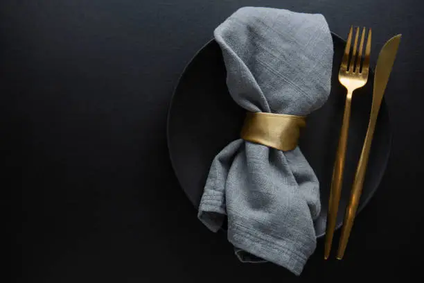 Golden cutlery with textile on plate on dark background. Top View.