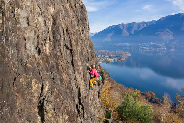 若い女性のロッククライマーは、急な登山、壮大な山の湖の景色につながります - conquering adversity endurance adventure danger ストックフォトと画像