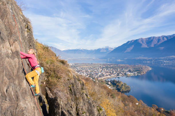 若い女性のロッククライマーは、急な登山、壮大な山の湖の景色につながります - conquering adversity endurance adventure danger ストックフォトと画像