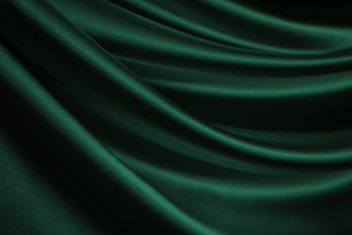 Dark green silk satin velvet. Nice soft folds. Shiny fabric. Wavy lines. Elegant background for design.