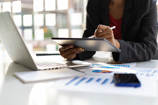 Modern business man holding tablet working on laptop in office. Businesswoman analyzing business strategy, planning finances and investing.