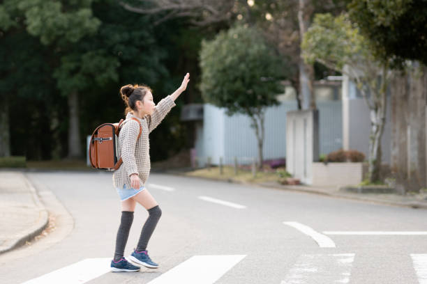 女の子は彼女の手を上げ、横断歩道を渡る - ランドセル ストックフォトと画像