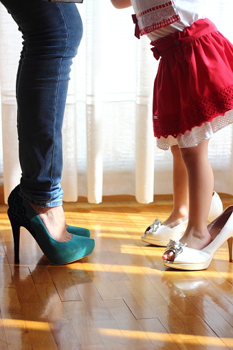 mother and daughter are copied. The mother wears high heels and the daughter imitates her. both stand to each other as a support. The affection is noticeable between the two. Only the legs are visible.