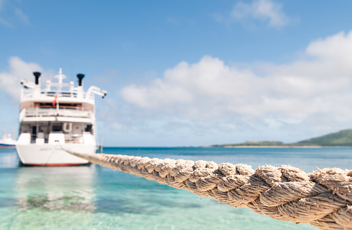 A long rope holding a boat moored off a beach in Fiji. Close-up focus on the foreground rope, with the boat defocused.
