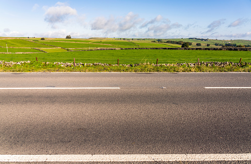 A side view of an empty section of road in the Peak District, with fields of grass up to the horizon in the background.