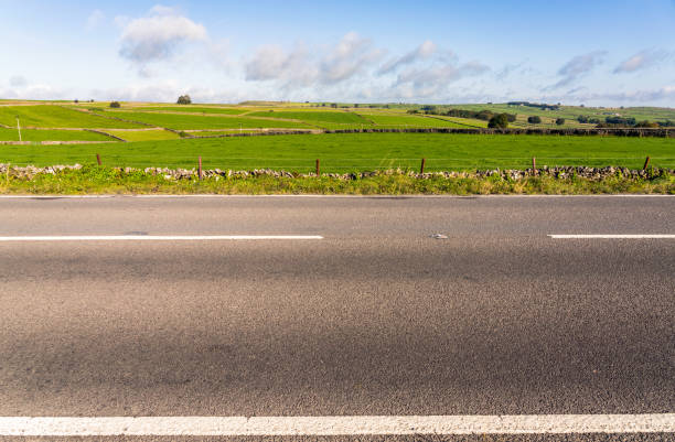 Empty English rural road - side view A side view of an empty section of road in the Peak District, with fields of grass up to the horizon in the background. roadside stock pictures, royalty-free photos & images