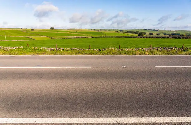 A side view of an empty section of road in the Peak District, with fields of grass up to the horizon in the background.