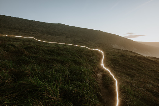 Light trail from a hiker's lantern, walking over a path after sunset