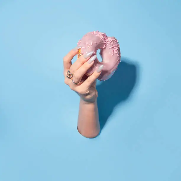 Photo of Sweet dessert, a donut in pink glaze in your hand.