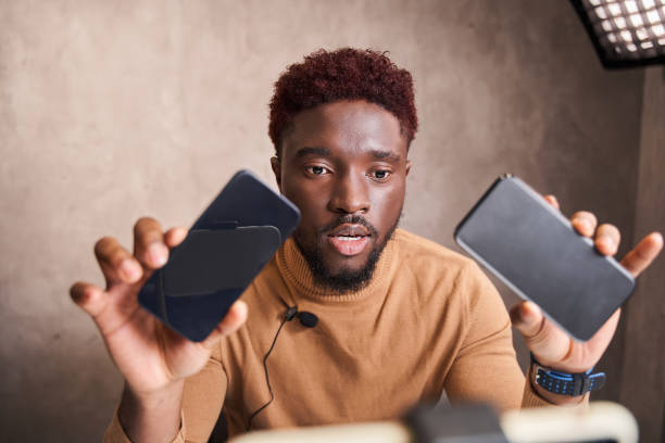 istock Multiracial man blogger showing two different smartphones and talking on video shooting 1361925236