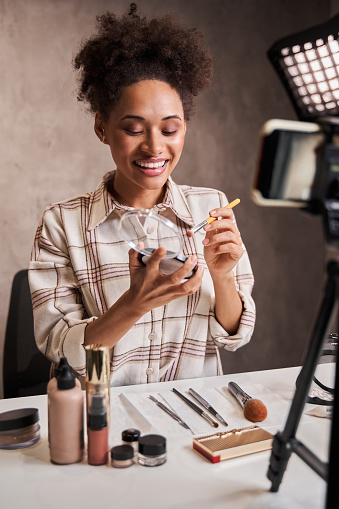 Vertical shot of the young woman talking about cosmetics while holding makeup palette and recording her video. Woman making tutorial for her blog