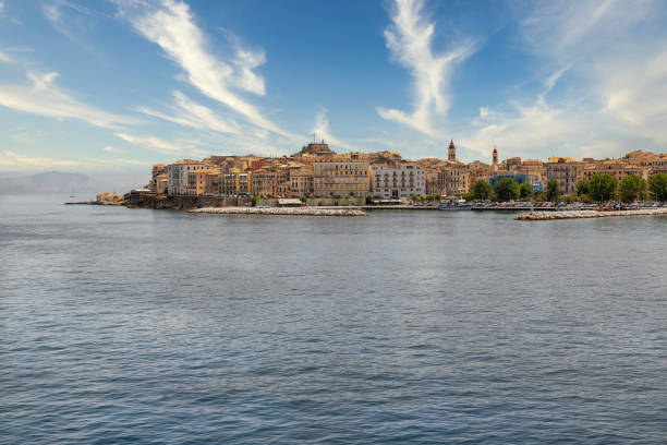 Kerkyra cityscape. Corfu island, Greece. Sea bay with calm turquoise water, colorful old houses, blue sky with white clouds.