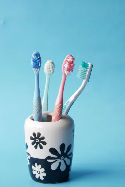 escovas de dentes coloridas em caneca branca contra fundo azul - toothbrush plastic multi colored hygiene - fotografias e filmes do acervo