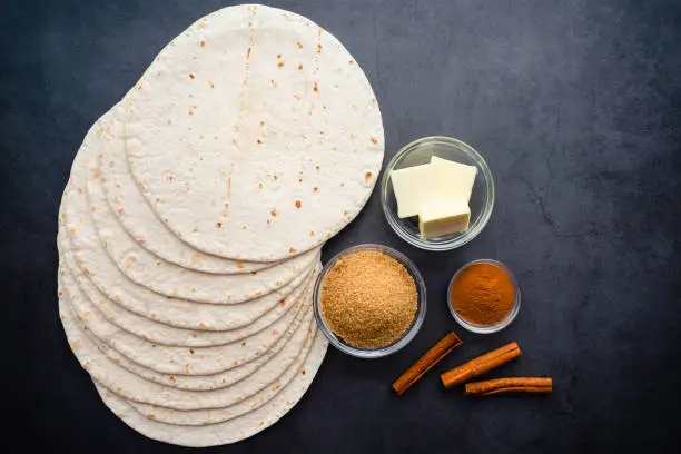 Flour tortillas, butter, brown sugar, and cinnamon on a dark background