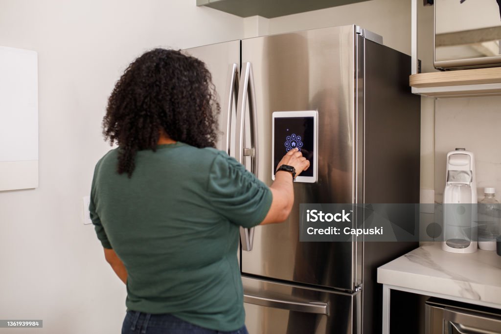 Young woman checking information from smart fridge Family interacting with smart home devices on daily activities Refrigerator Stock Photo
