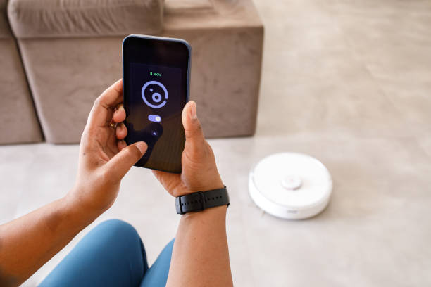istock Young woman using smartphone to control smart vacuum cleaner robot 1361939995