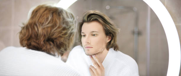 istock young man looking in the mirror,combing his hair,looking at problems on face. 1361941534