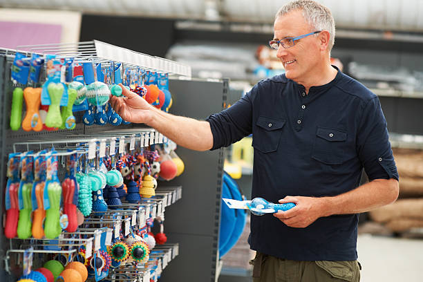 Shopping for his puppy Portrait of a mature man selecting some colourful dog toys from the pet store pet shop photos stock pictures, royalty-free photos & images