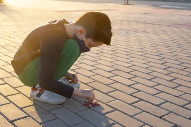 Photo of Squatting boy playing with firecrackers wearing facemask for covid protection