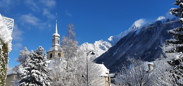 Aerial view of a quaint snow-covered village with a church spire, surrounded by winter trees.