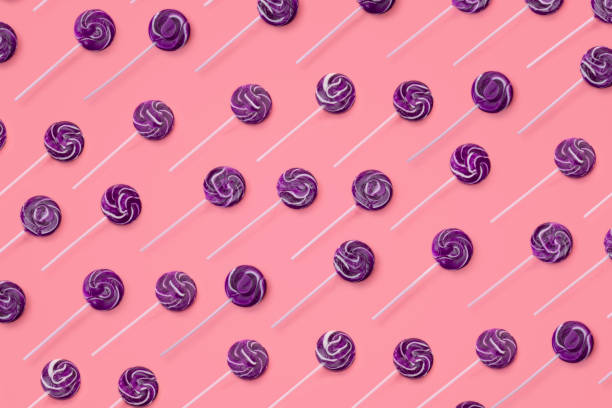 This is a repetitive pattern of colorful purple swirl lollipops on a pink background