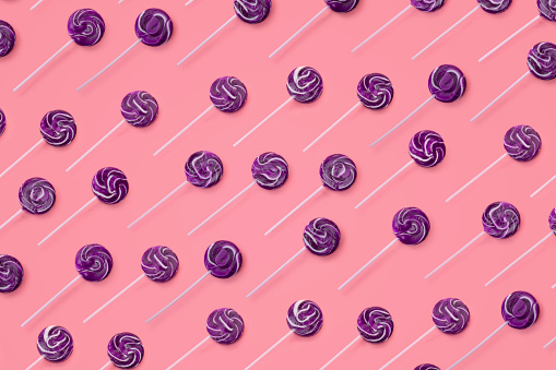 This is a repetitive pattern of colorful purple swirl lollipops on a pink background