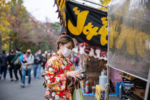 Young woman in kimono buying food at food stall in matsuri