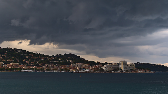 Beautiful view of town Sainte-Maxime, a popular holiday destination at the French Riviera, on stormy day in autumn season with thuderstorm clouds above the buildings of the city and mediterranean sea.