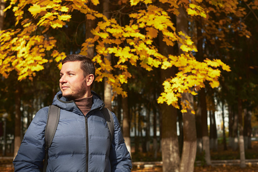 Portrait of handsome man in the autumn forest in a down jacket and scarf. Front view.