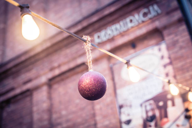 Christmas bauble hangs on a garland of light bulbs in the garden, one of the restaurants in Krakow. Townhouses in the background