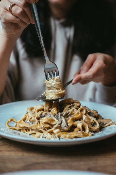 donna che mangia pasta con salsa di panna e funghi - pasta noodles tagliatelle freshness foto e immagini stock