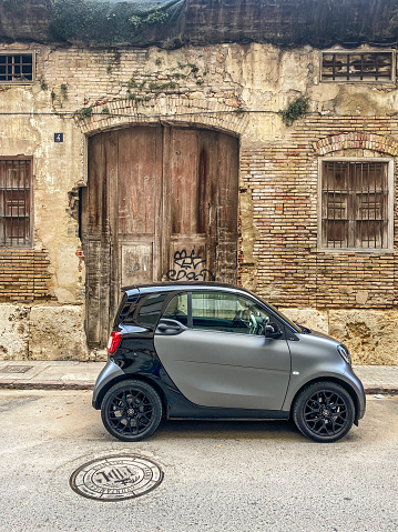 Valencia, Spain - June 29, 2021: Compact car model Smart parked in the street next to old deteriorated construction. Some places in the city never changed and stay like in the past