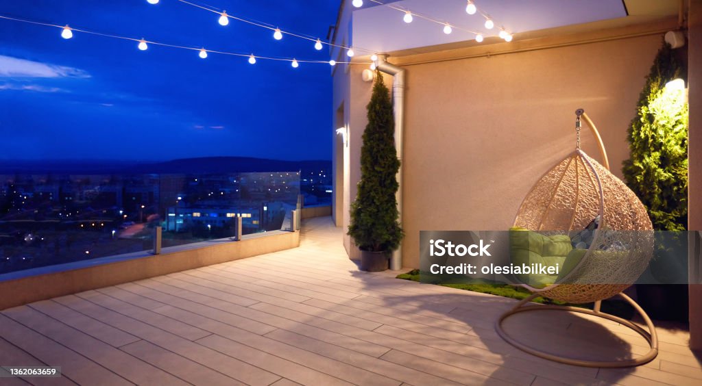 cozy rooftop terrace with rattan hanging chair, garlands and beautiful landscape at night Back Yard Stock Photo