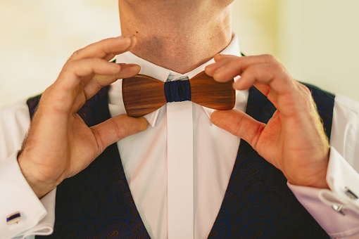 Groom morning preparation. Bearded groom getting dressed in wedding shirt with wooden bow tie