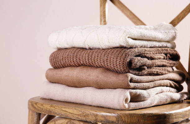 istock Stack of folded warm sweaters on wooden chair against light background 1362069658