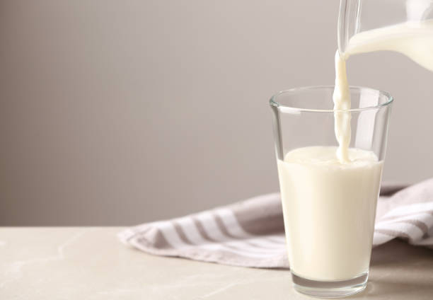 istock Pouring milk into glass on table against grey background. Space for text 1362071801