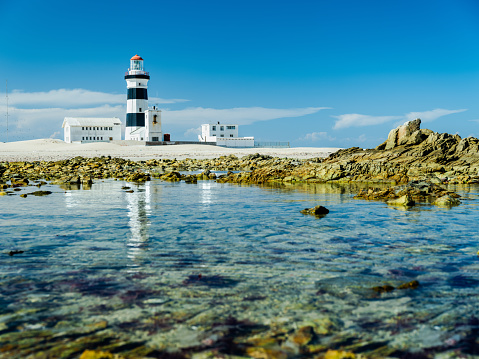 Landscape shot of cape recife lighthouse with reflection in the water on a clear blue sky day in summer