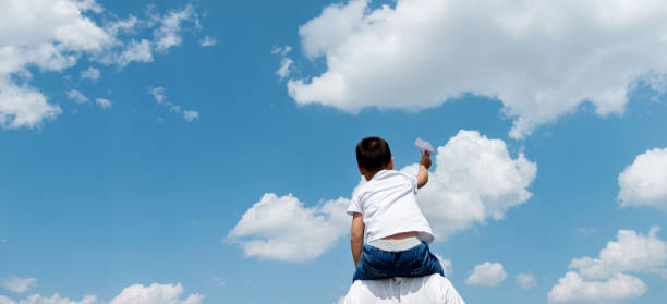 istock Boy sitting on father's shoulder playing paper airplane 1362075183
