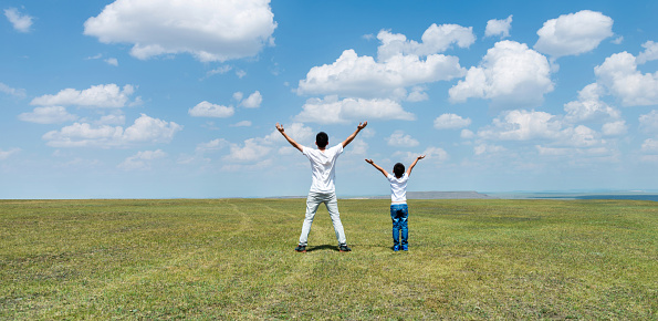 Father and son standing in meadow with arms outstretched.