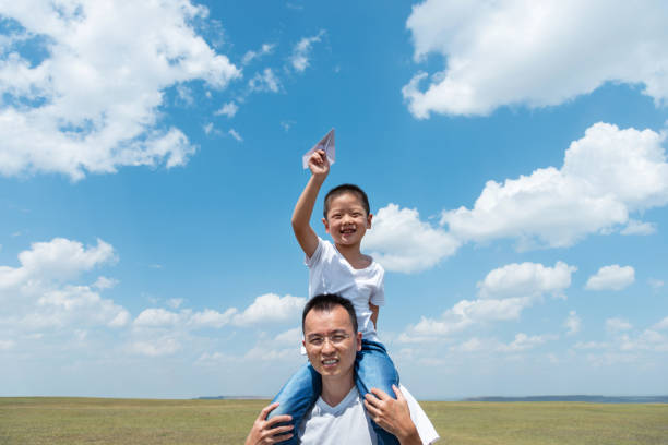 istock Boy sitting on father's shoulder playing paper airplane 1362075190