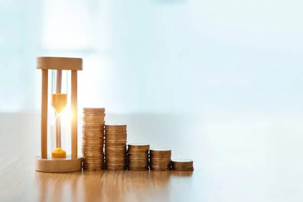 Photo of Hourglass and coins on wooden table